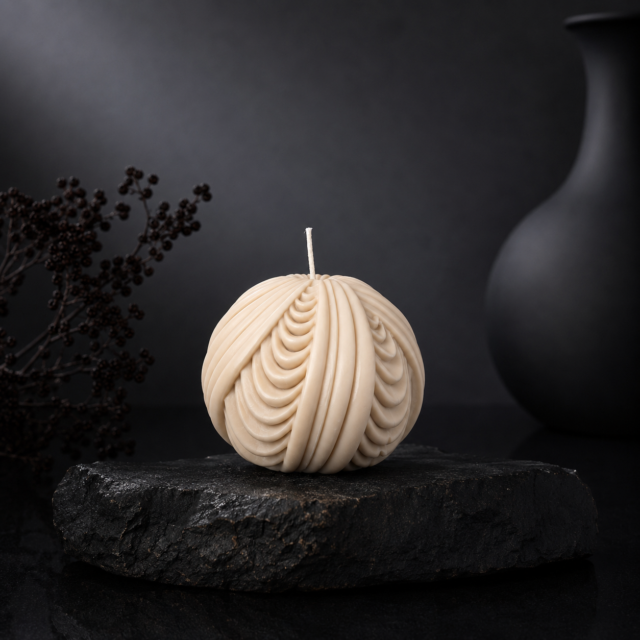 Obsidian Sphere sculptural candle in warm cashmere neutral tone displayed on a charcoal stone plinth against a dark editorial backdrop.