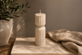 Cashmere Vestige Column sculptural soy candle styled on a stone table beside a textured black vase in a warm luxury interior.