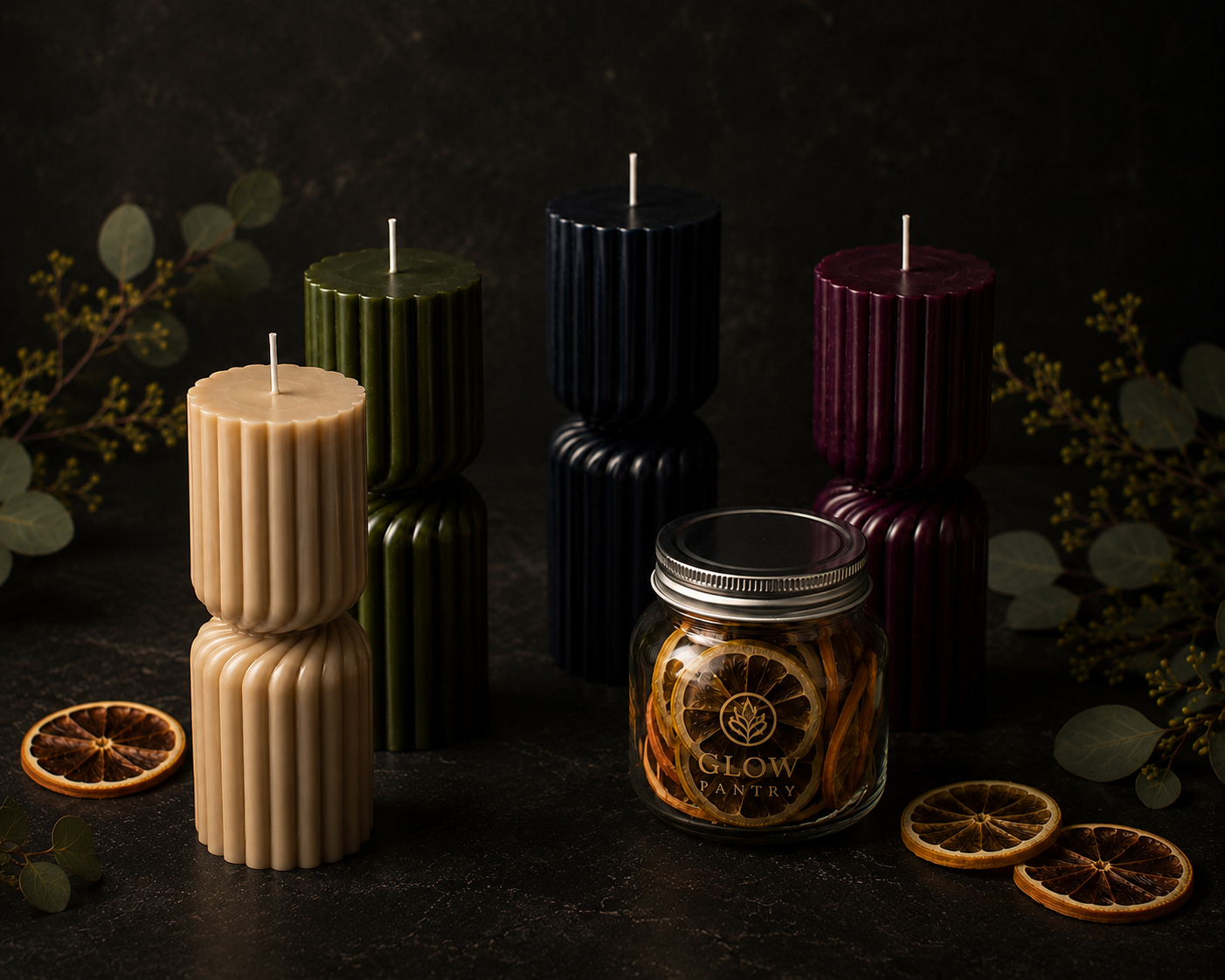 Glow Pantry sculptural candles in Cashmere, Moss, Midnight and Mulberry alongside a jar of Citrus Medley dried fruit, styled with dried citrus and eucalyptus in a luxury dark-toned product photograph.
