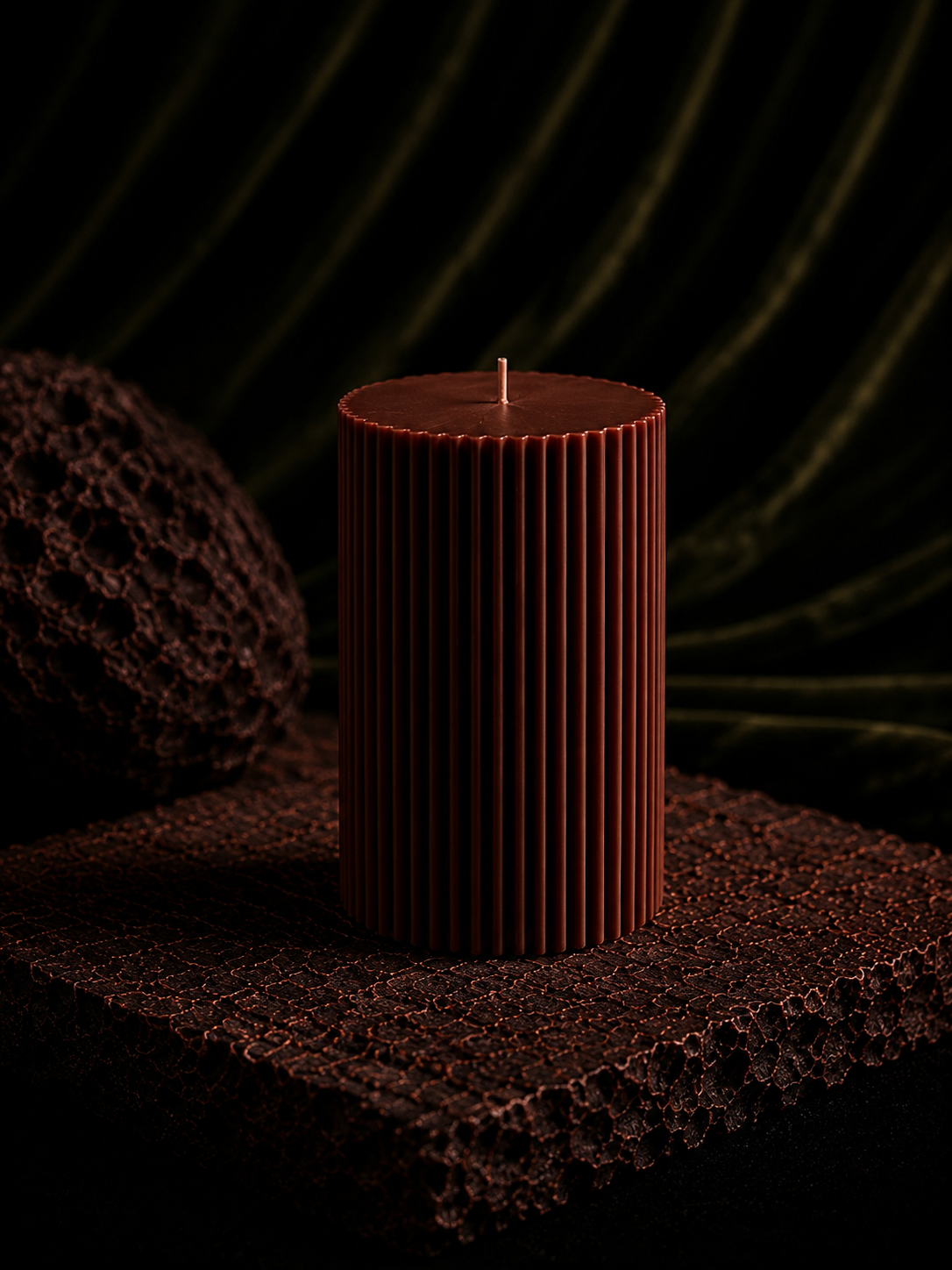 Glow Pantry Atelier Grand sculptural pillar candle in Ember, displayed on a textured stone plinth with warm moody lighting and an elegant botanical backdrop.
