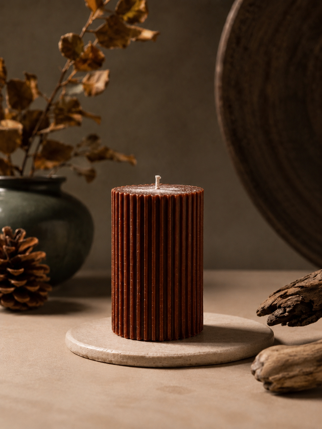 Glow Pantry Atelier Petit sculptural pillar candle in Ember, styled on a travertine pedestal with warm earthy décor, dried foliage and driftwood in a luxury lifestyle setting.