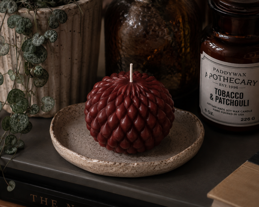 Ember Obsidian Bloom soy wax candle in deep terracotta, styled on a ceramic dish with layered textures and moody interior decor.