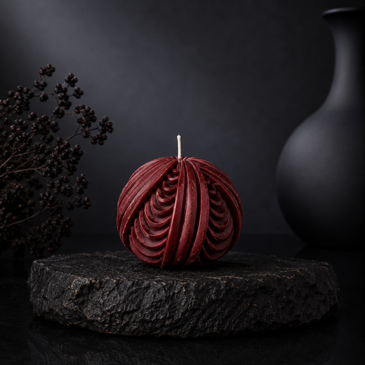 Obsidian Sphere sculptural candle in deep burnt terracotta tone displayed on a charcoal stone plinth against a dark editorial backdrop.