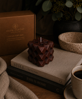 Ember Discovery Cube geometric sculptural candle displayed on stacked books alongside ceramic vessels and botanical details, with The Collector’s Box in the background.