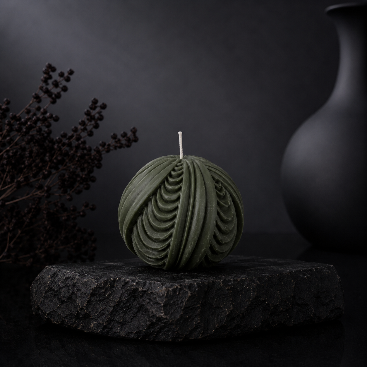 Obsidian Sphere sculptural candle in deep moss green displayed on a charcoal stone plinth against a dark editorial backdrop.