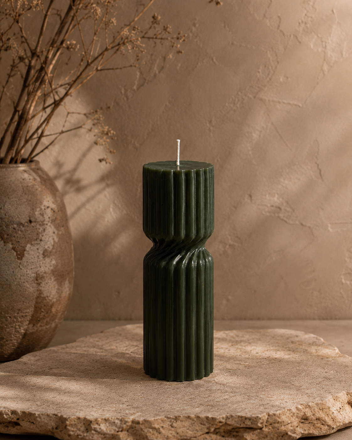Moss Vestige Column sculptural soy candle styled on a stone table beside a textured brown vase in a warm luxury exterior.