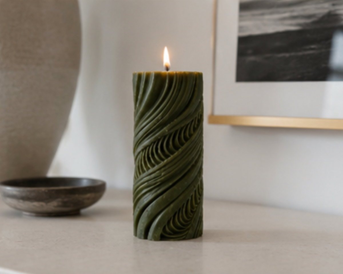 Lit Moss Obsidian Current sculptural pillar candle styled on a modern console with earthy ceramics and framed artwork.