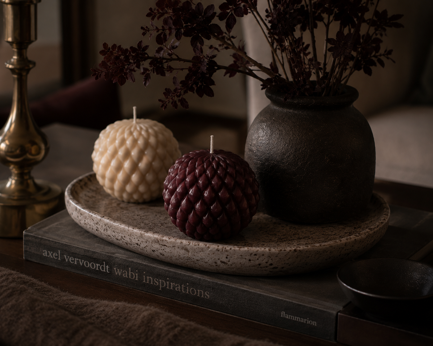 Mulberry and Cashmere Obsidian Bloom sculptural candles displayed on a stone tray beside a textured vase, creating a warm and layered interior vignette.