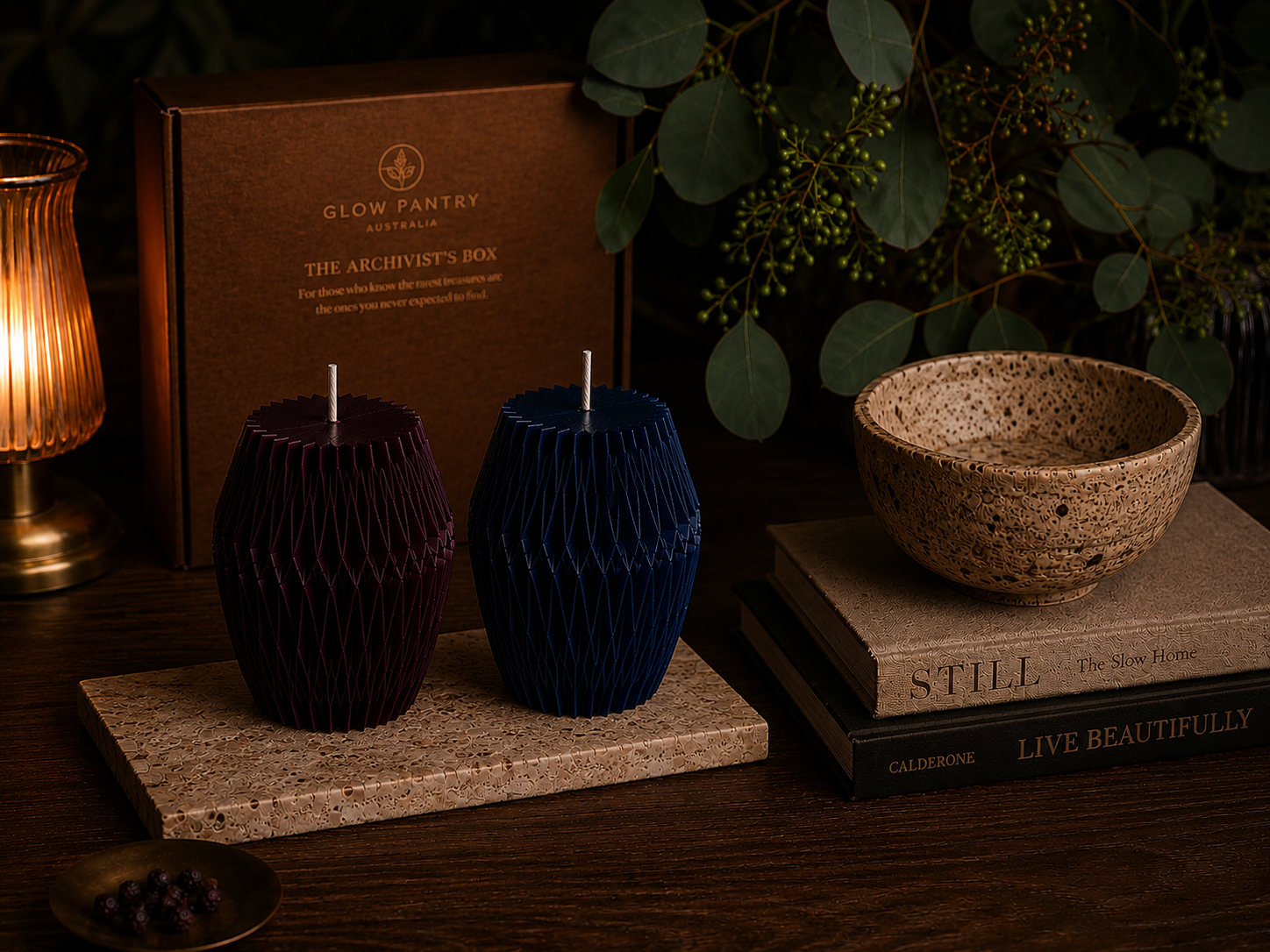 Mulberry and Midnight Facet sculptural candles presented in a richly layered interior scene with stone, ceramic and botanical elements, accompanied by The Archivist’s Box and warm ambient lighting.