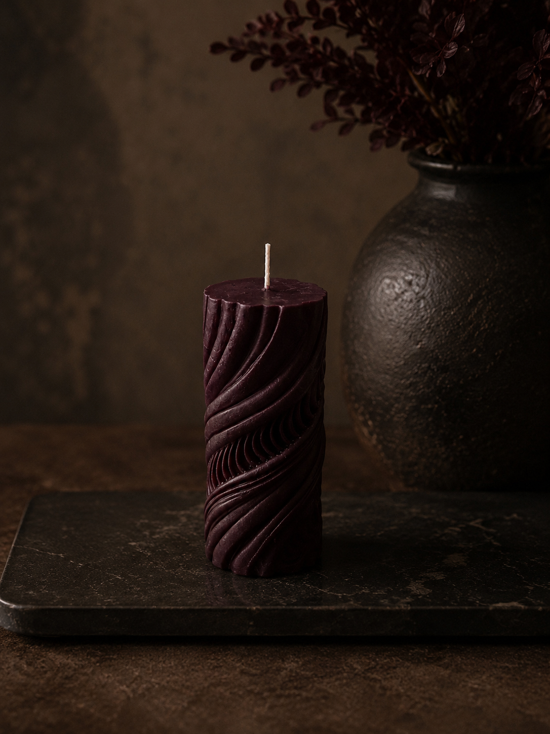 Mulberry Obsidian Current sculptural pillar candle displayed on a black stone plinth beside a textured black vase. Hand-poured soy wax candle from Glow Pantry’s Lowlight Series.