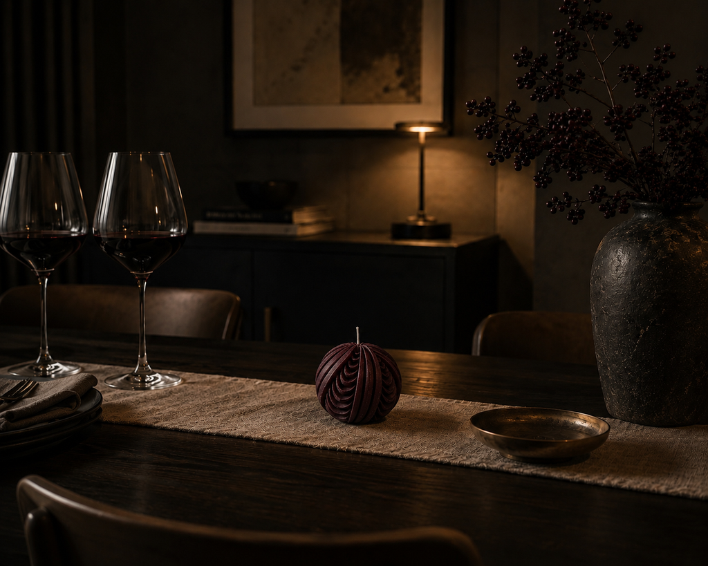 Deep mulberry Obsidian Sphere candle displayed on a dining table with wine glasses and brass accents, creating an intimate, softly lit atmosphere.