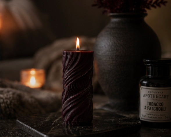 Mulberry Obsidian Current sculptural pillar candle burning in a low-light interior with black ceramic decor and warm candlelight.