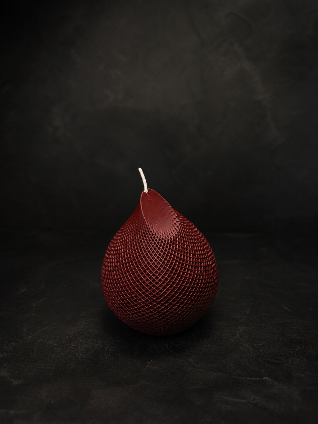 Obsidian Drop candle in Ember — hand-poured deep red sculptural wax piece with textured lattice surface, styled as a moody art object.