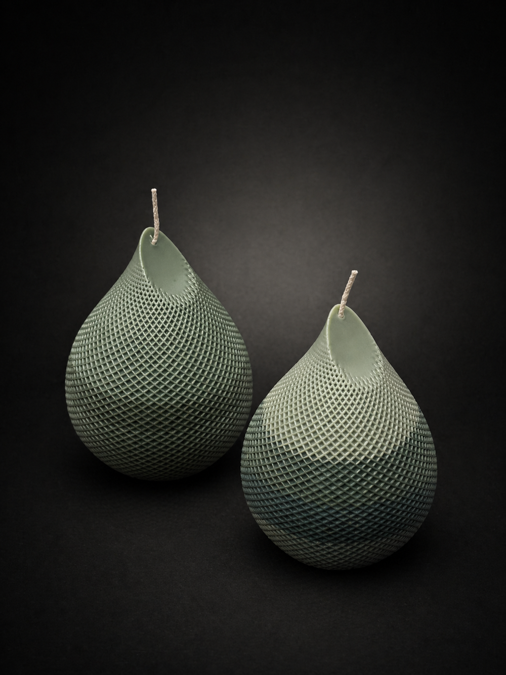 Pair of Obsidian Drop candles in Moss tone — sculptural wax pieces with intricate lattice texture, styled together as lowlight art objects. Moss tone with subtle tonal variation from deep olive to lighter sage