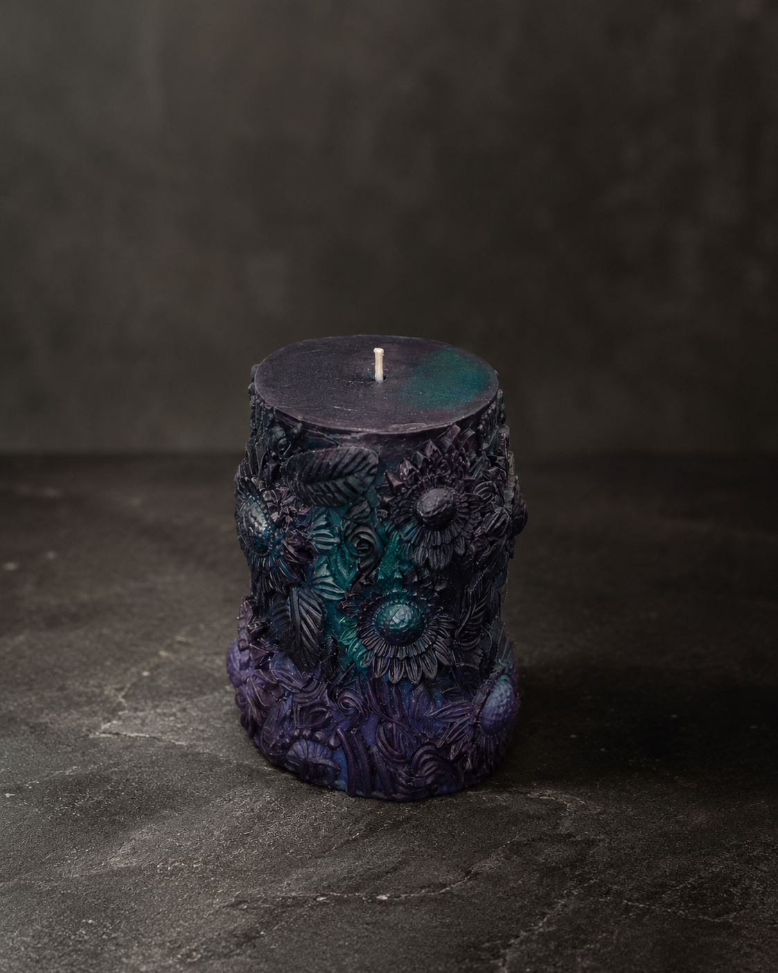 The Alchemist Relic edition sculptural candle featuring deep purple, black, and teal tones with intricate floral detailing on a dramatic editorial backdrop.