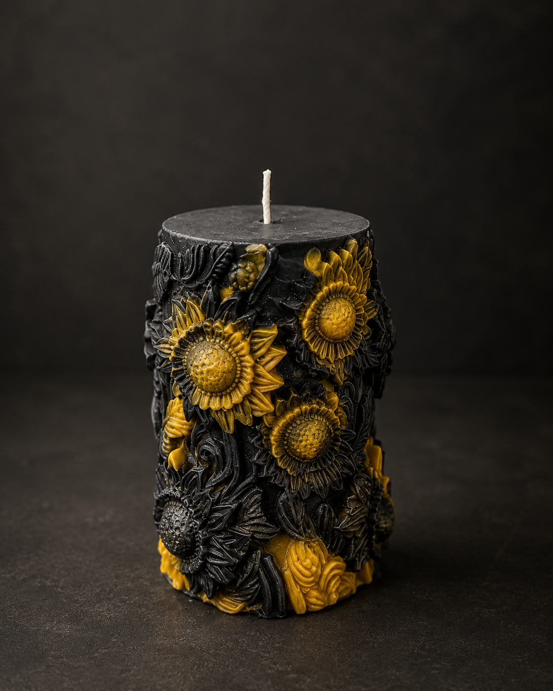 The Alchemist sculptural candle in yellow and black with intricate sunflower detailing against dark wax, photographed on a moody editorial background.
