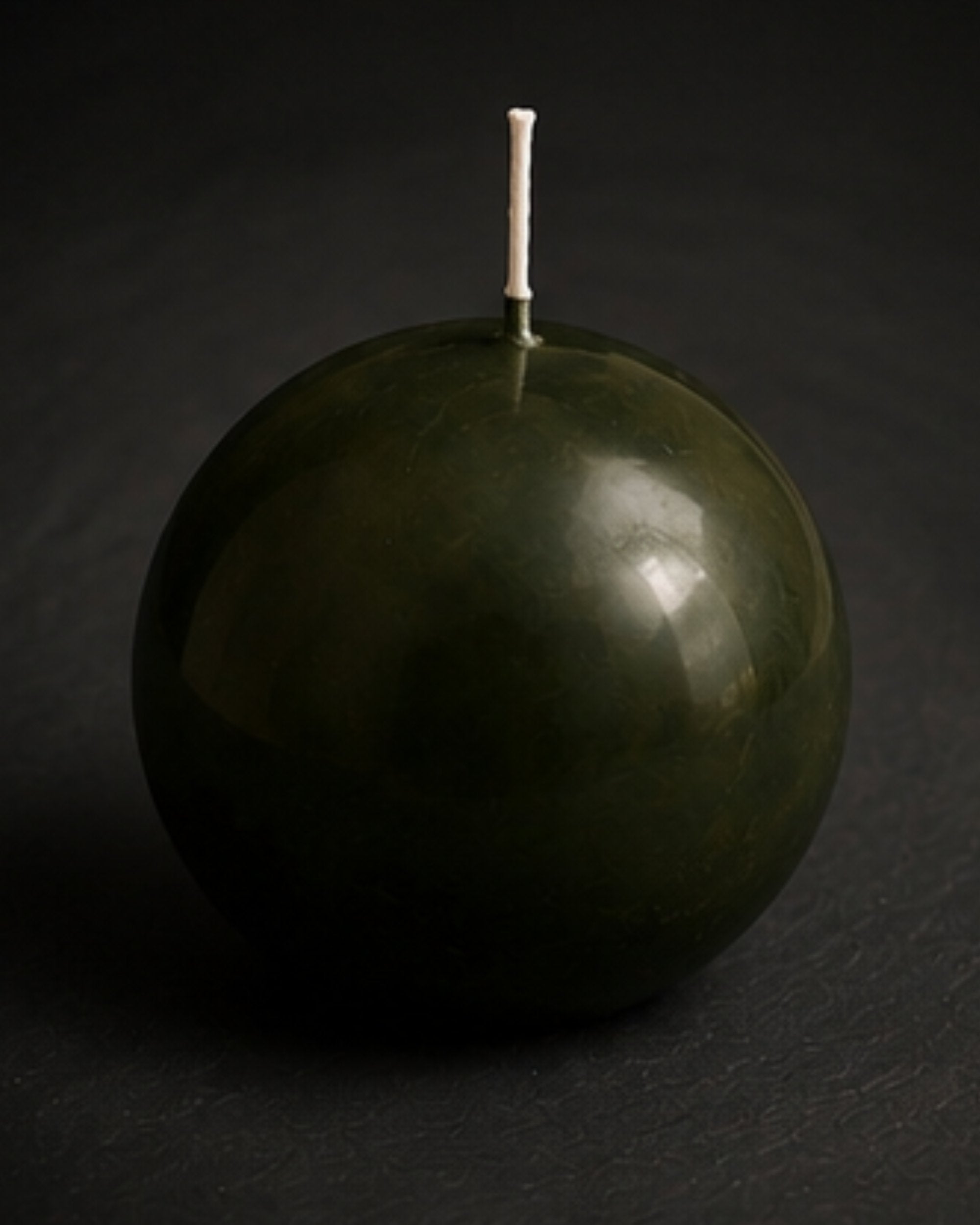 Verdant Orb sculptural sphere candle in deep moss green tones against a charcoal editorial background.