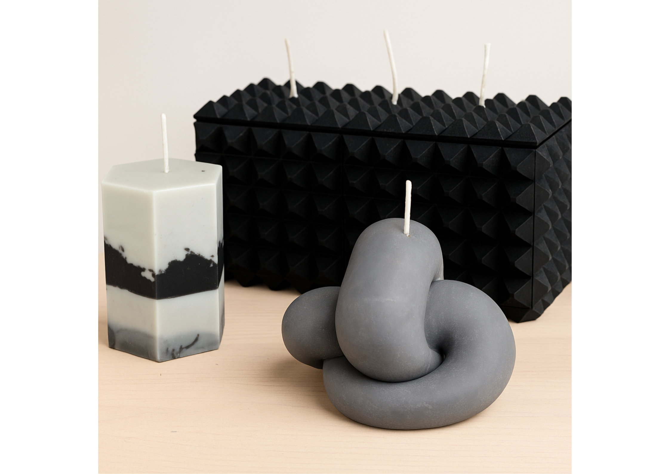 The Gordian Knot sculptural candle displayed alongside geometric black sculptural candles in a curated editorial arrangement.